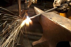A metal fabricator utilizing a torch to heat up a piece of metal in order to shape it.