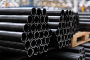 Many black pipes stacked on pallets in a warehouse.