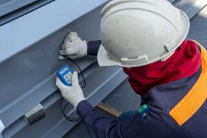 Man with a hard hat testing fabricated steel with a device