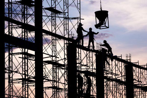 Silhouette of construction workers on scaffolding at sunset.