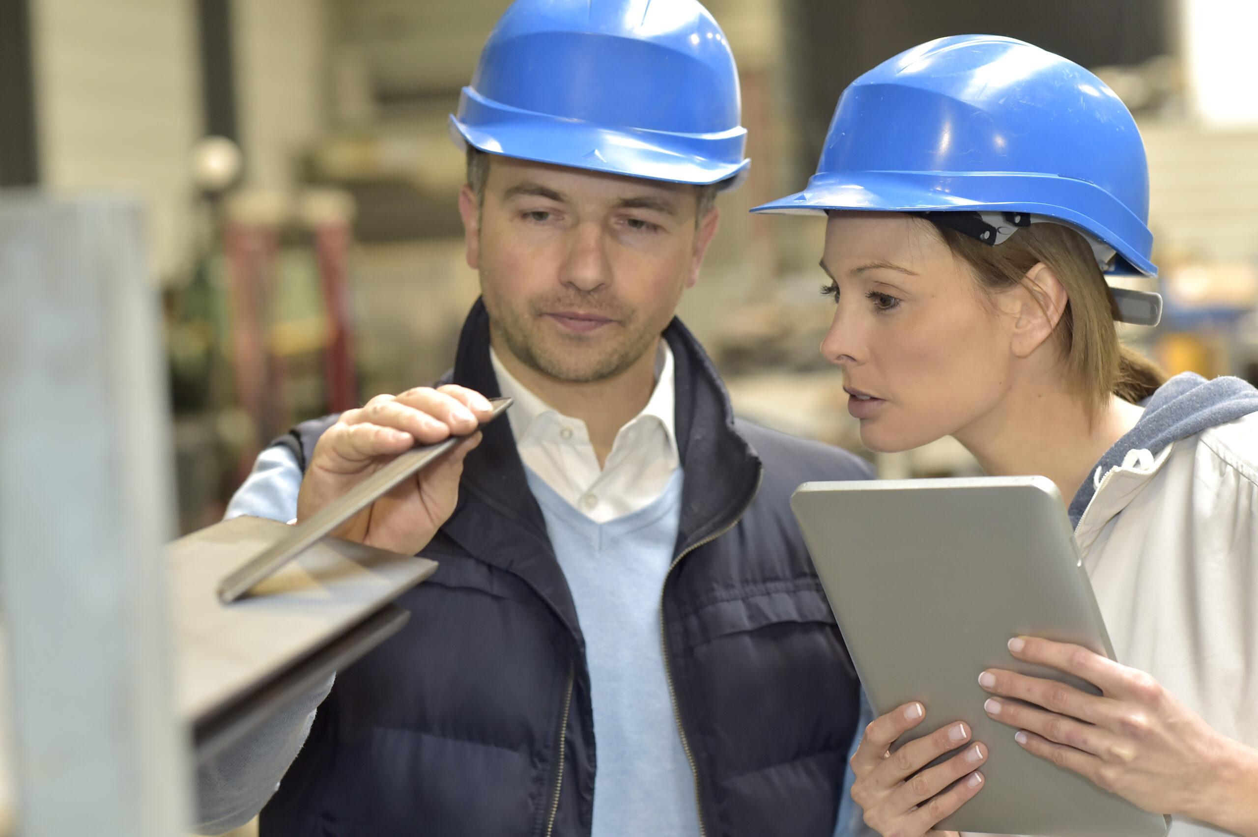 Two people discussing steel wearing hard hats