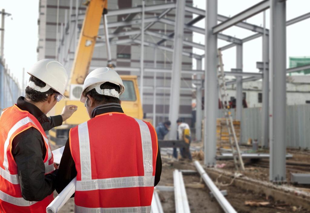 two builders discussing a plan in front of a steal structure