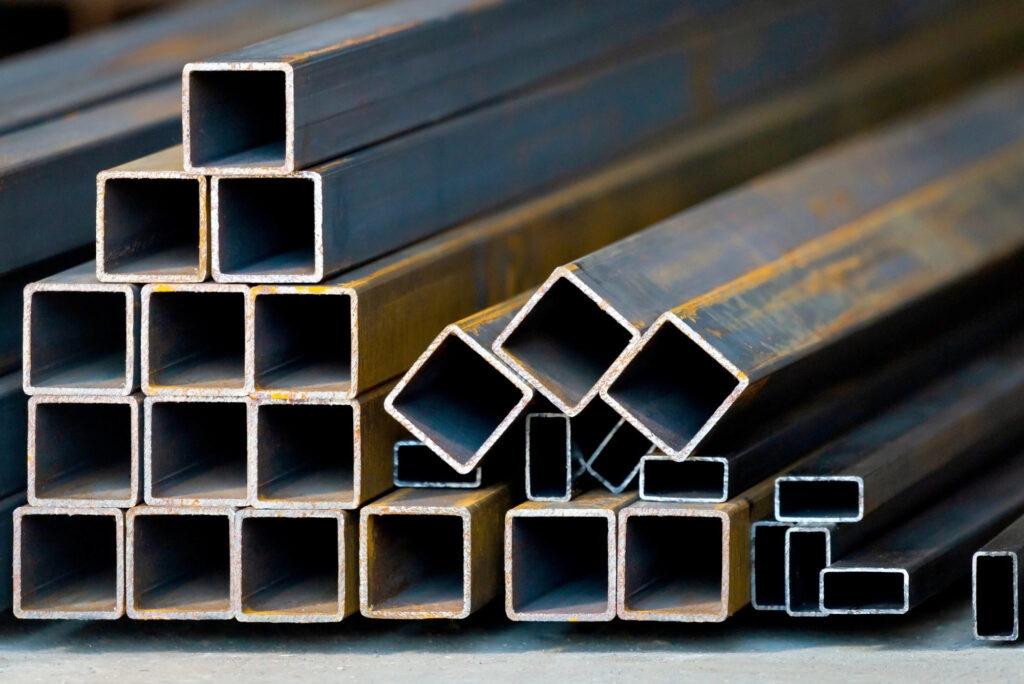 Stacks of steel rectangular tubes in various sizes are arranged on a concrete floor.
