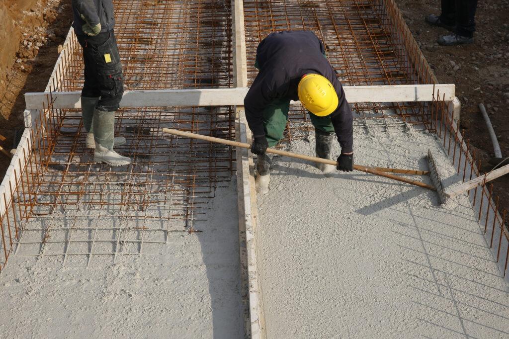 Construction workers pouring concrete over reinforced foundations