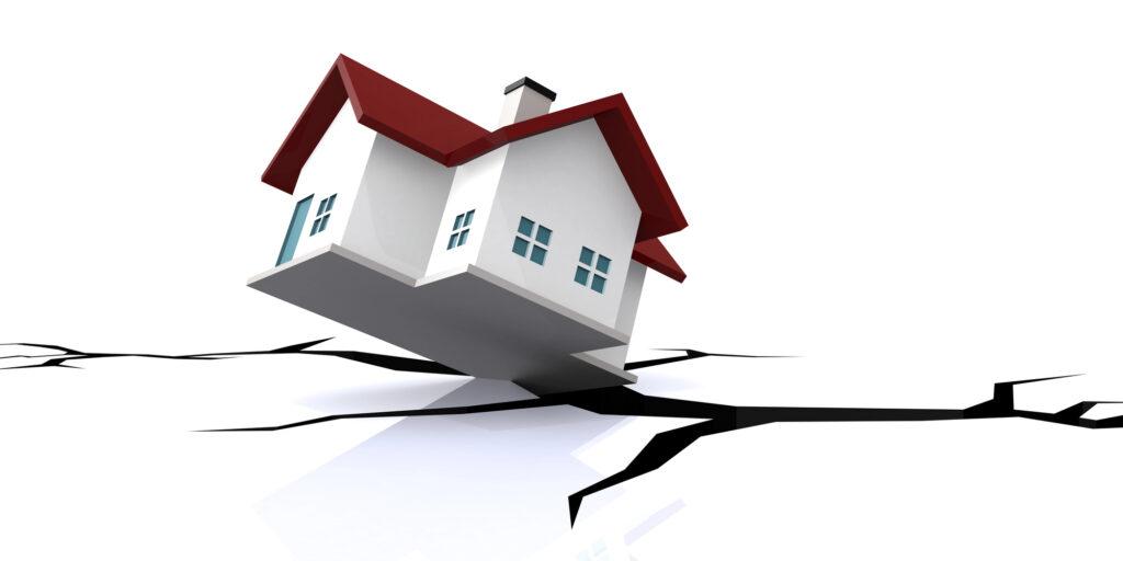 A house tilts above large cracks in the ground, suggesting earthquake damage or instability.