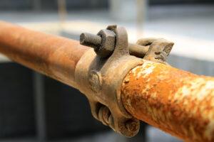 A close-up of a rusty metal pipe joint with a bolt and clamp outdoors.